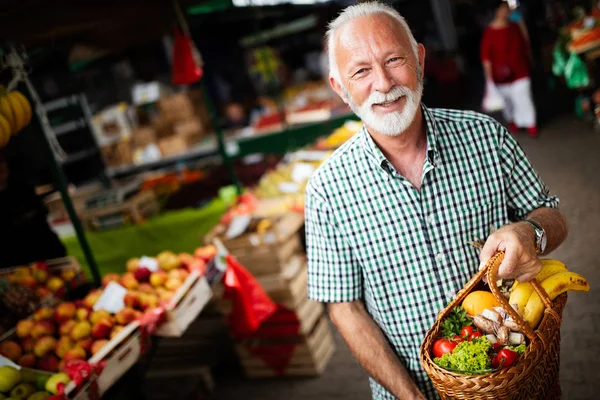 Handsome senior man shopping for fresh vegetable and fruit in a market