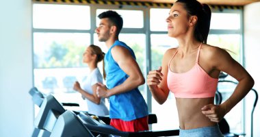 Spor salonunda koşu bandında kardiyo antrenmanı yapan insanların fotoğrafı.