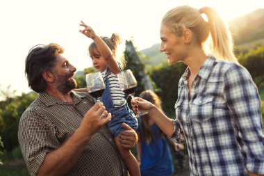 Üzüm bağında kırmızı şarap içip eğlenen insanların fotoğrafı.
