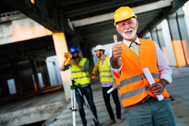 Mühendis, müteahhit, mimar, yatırımcı takım çalışması. Konuşan ve planlayan bir grup inşaat işçisi, ellerinde planlar var.