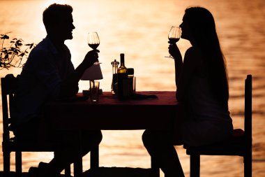 Genç çift, tropik bir tatil köyünde romantik bir gün batımı yemeği yiyor.