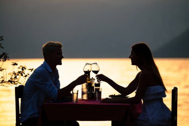 İnsanlar, kutlama, tatil, balayı ve romantizm konsepti. Genç çift sahilde romantik bir akşam yemeği yiyor..