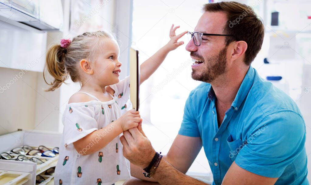 Health care, eyesight and vision concept. Happy kid choosing glasses with her father at optics store