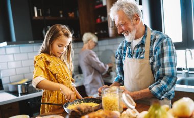 Gülümseyen mutlu büyükbaba çocuklara mutfakta yemek yapmaları için yardım ediyor.