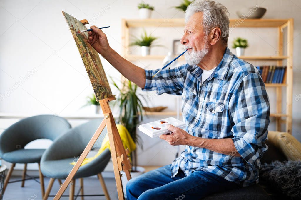 Smiling senior man painting on canvas at home