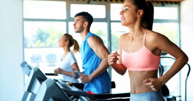 Spor salonundaki koşu bandında çalışan ve gülümseyen insanlar.