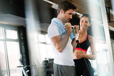 Sporty fit man doing weight exercises with assistance of her personal trainer