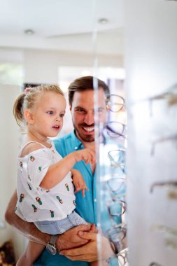 Sağlık hizmeti, görme ve görme konsepti. Babası ile optik mağazasında gözlük seçen mutlu bir çocuk.