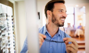 Optik mağazasında gözlük seçen yakışıklı genç adam..