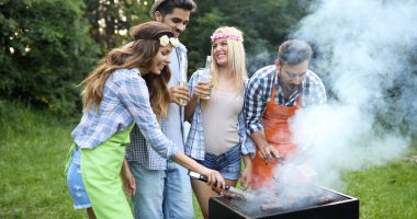 Neşeli arkadaşlar doğada vakit geçirip barbekü yapıyorlar.