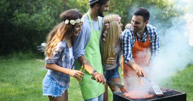 Arkadaşlar barbekü yapıyor ve doğada öğle yemeği yiyorlar.