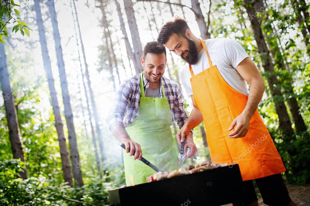 Leisure, food, people and holidays concept. Men cooking meat on barbecue grill at outdoor summer party