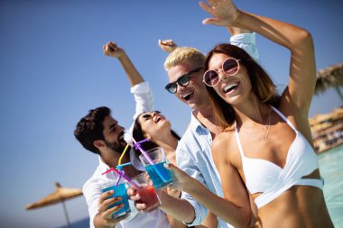 Bir grup mutlu arkadaş havuzda kokteyllerle dans ediyor.