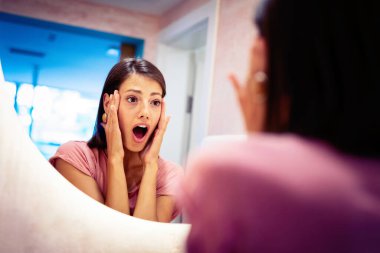 Yüzündeki kırışıklıklar yüzünden endişelenen bir kadının ayna yansıması.