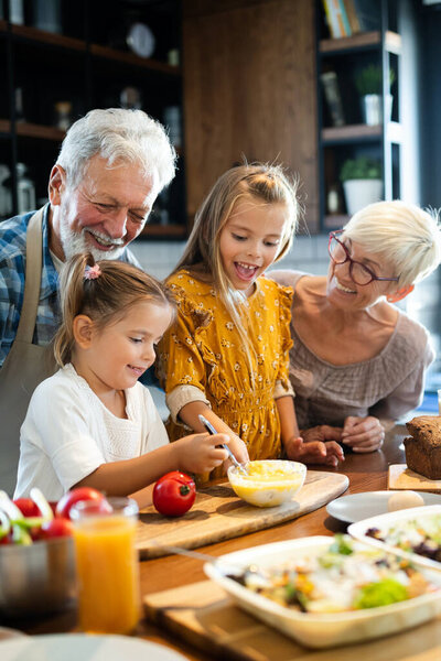 Smiling happy grandfather helping children to cook in the kitchen