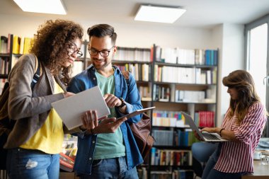 Üniversite öğrencileri kütüphanedeki görevleriyle işbirliği içinde. Kitap okuyan bir grup genç..