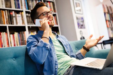 Zevkle çalışıyorum. Cep telefonuyla konuşan ve dizüstü bilgisayarına bakan mutlu genç adam.
