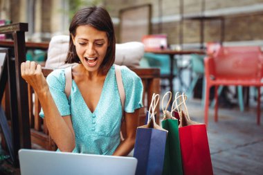 Dışarıda dizüstü bilgisayarda iyi haberler okuyan heyecanlı bir kadın.