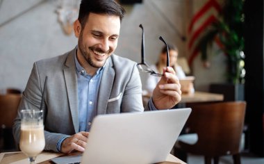 Ofiste dizüstü bilgisayar kullanarak çalışan yakışıklı, kendine güvenen iş adamı.