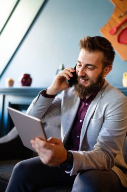 İşinden zevk alıyor. Mutlu genç sakallı iş adamı cep telefonuyla konuşuyor.