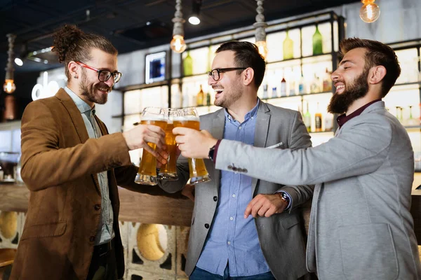 Happy business people drink beer after work in pub. Businessmen enjoy a beer.
