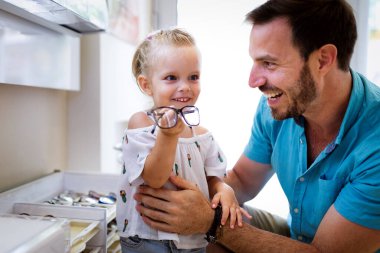 Sağlık hizmeti, görme ve görme konsepti. Babası ile optik mağazasında gözlük seçen mutlu bir çocuk.
