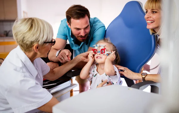 眼科医は現代のクリニックで可愛い女の子の目のビジョンをチェックしています 眼科クリニックの娘を持つ家族 — ストック写真