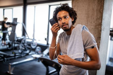 Spor salonunda cep telefonu kullanan genç kaslı adam.