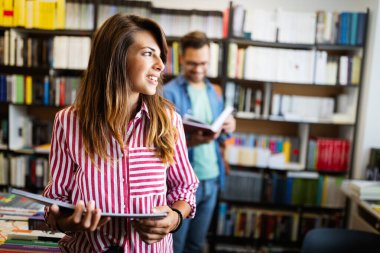 Eğitim, lise, üniversite, öğrenme ve insanların konsepti. Gülümseyen mutlu öğrenci kız kütüphanede kitap okuyor.