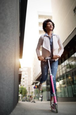 Sokakta elektrikli scooter süren mutlu güzel bir kadın.