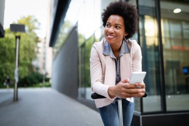 Scooter 'ın yanında duran ve şehirde cep telefonu kullanan mutlu kadın.