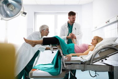 Hastanede doğum yapan genç ve güzel bir kadın doğum yapmak için bastırıyor, doğum uzmanları yardım ediyor.