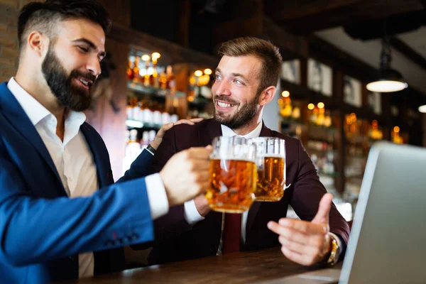 Handsome young businessmen drinking beer, talking and smiling while resting at the pub