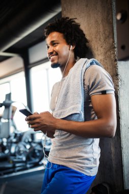 Spor salonunda egzersiz yaparken telefonu kullanan yakışıklı bir genç.