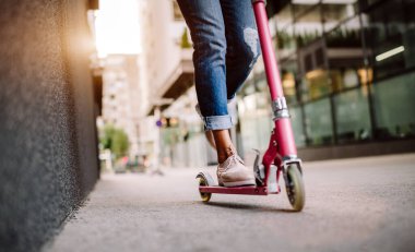 Ofis binasının arka planında elektrikli scooter kullanan mutlu kadın.
