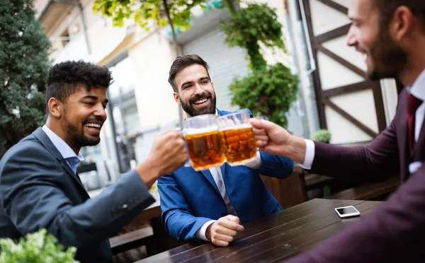 Cheerful old friends, business man having fun and drinking beer at bar counter in pub.