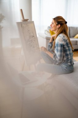 Mutlu genç kadın atölyede tuvale resim yapıyor.