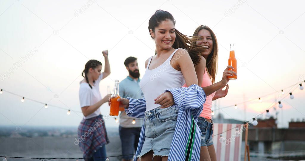 Group of friends having fun, dancing and drinking cocktails outdoor on a rooftop get together