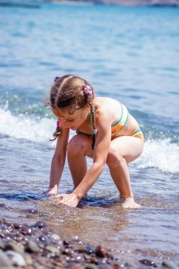 Kız çocuk sahilde çakıl taşları toplama.