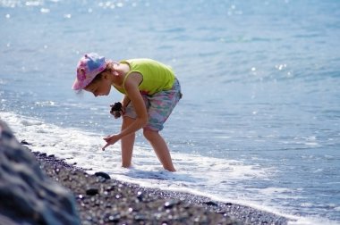 Kız çocuk sahilde çakıl taşları toplama.