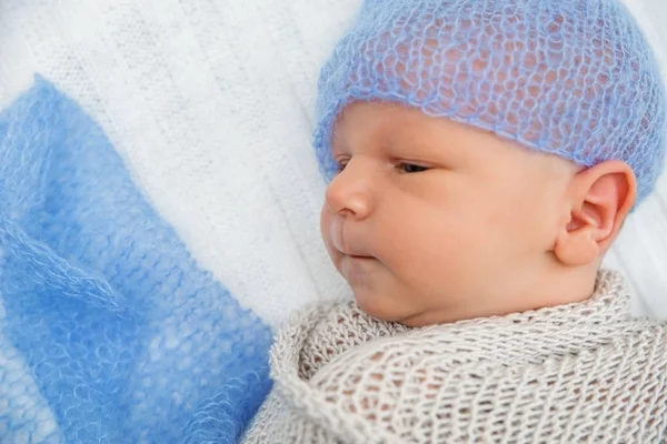 Een pasgeboren baby verpakt in een gebreide deken en blauwe gebreide cap. — Stockfoto