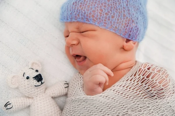 Новорожденный ребенок, завернутый в трикотажное одеяло и синюю вязаную шапочку . — стоковое фото