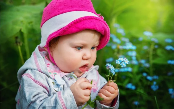 Bebê menina sentada em alta grama verde e está segurando flores . — Fotografia de Stock