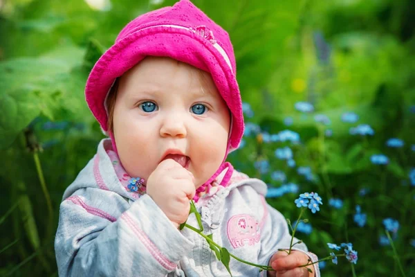Bebê menina sentada em alta grama verde e está segurando flores . — Fotografia de Stock
