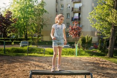 Bir yerleşim bölgesinde bir bankta atlama tulum kız çocuk.