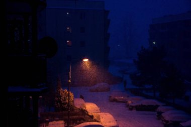 Bir kış akşamı sokakta bir fener ışığında yağan kar.