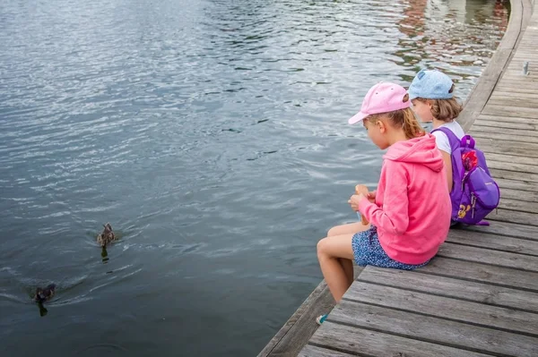 İskelede oturan iki çocuk su yakınındaki ve ördeklere yem.