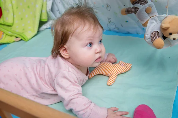 The baby plays with toys in her crib.