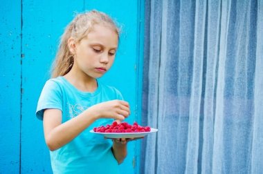 Ahududu çiftlik duvarın yanında bir tabak ile çocuk.
