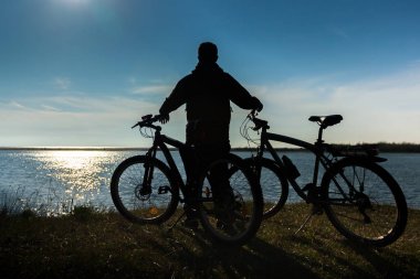 Yalnız bir adam bisiklet'nde günbatımı rahatlatıcı ile gökyüzü deniz, nehir
